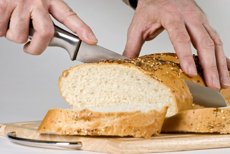 A man with long knife slicing through a large loaf of bread. 