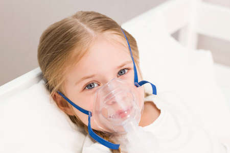 girl is breathing through an inhaler. a sick child is lying on the bedの写真素材