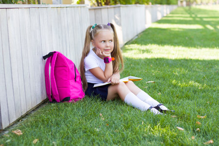 girl with a backpack is sitting on the lawn.First day of schoolの写真素材
