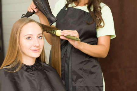 young woman is drying her hair with a hair dryerの写真素材