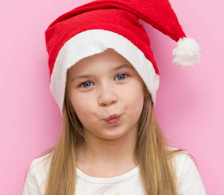 little girl in a red Christmas hat presents a red box with a gold bow, a gift. Smiles. The new year is 2021. Close upの写真素材
