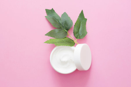a jar of face cream, a body with green, exotic leaves next to it, on a pink background. Natural...