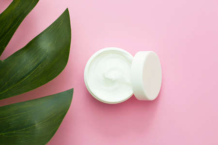 a jar of face cream, a body with green, exotic leaves next to it, on a pink background. Natural Care, Organic Cream, Moisturizing, Care, Beauty, Cosmetics Productionの写真素材