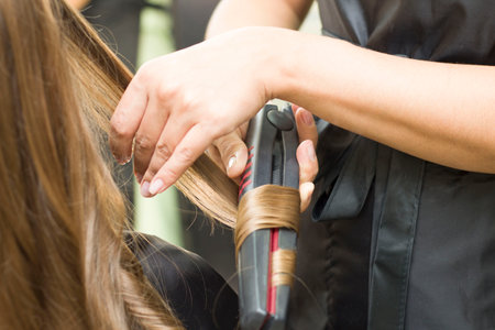a young woman straightens her hair with an ironの写真素材