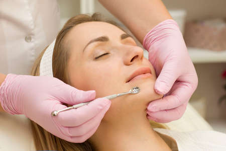 Procedure for cleaning skin with steel tool from blackheads and acne. Deep cleansing of the female face with blackhead remover in the beauty salon. Cosmetologist making receiving cleansing therapyの写真素材