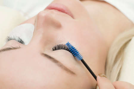 Eyelash extension procedure. young woman with long eyelashes in a beauty salon. Eyelashes close-up. brush in the hands of the masterの写真素材