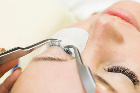 young woman is undergoing a close-up eyelash extension procedure. Eyelash extension tweezersの写真素材