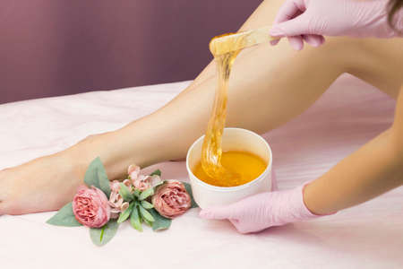 Hair removal in a luxury spa studio. Women's feet wax with saccharin. Hot sugar. The product of the wax bowl. Salon bank. Purple, lilac backgroundの写真素材