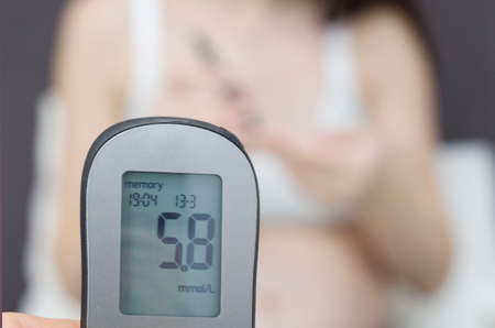 Diabetes of pregnant women. A pregnant woman with a stomach measures the level of glucose in the blood with a glucometer.の写真素材