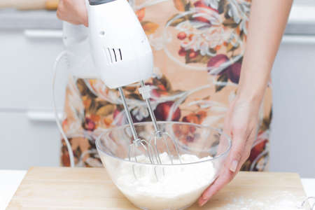 Young woman uses mixer in beating eggs, stands in a modern kitchenの写真素材