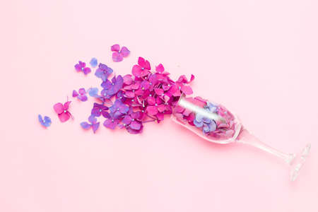 A champagne glass with spring flowers on a pink background, the concept of a party in a minimal season. The idea of the flowering of nature. Purple and pink flowersの写真素材