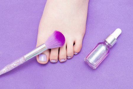 A leg on a purple background, next to a fluffy nail brush. Pedicure. Purple tone