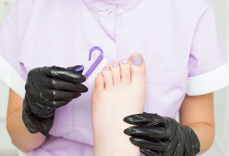 The master during the pedicure. The process of a professional pedicure. The concept of beauty and health. A nail brush. Purple, lilac colorの写真素材