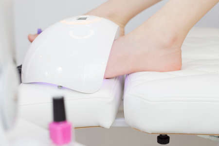 The pedicure master, after applying purple nail polish, dries them under an ultraviolet lamp. Lamp for drying nailsの写真素材