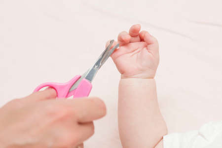 Mom gets a manicure with nail scissors and cuts her cute baby's nails while lying on the bed. The concept of child care.の写真素材