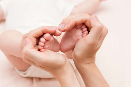 The baby's legs in the mother's hands are in the form of a hearth, a heartの写真素材