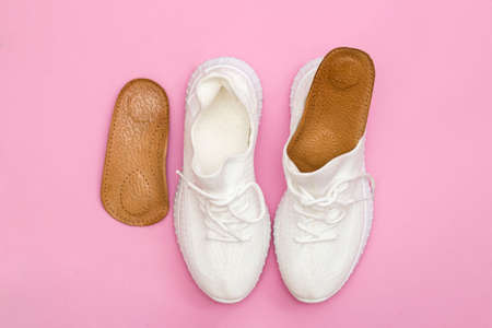 Brown orthopedic insoles for shoes. White sneakers on a pink background.の写真素材