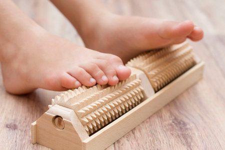 The girl does self-massage of the feet on a special wooden needle massager for the prevention of flat feet, valgus. Relaxation of the legs.の写真素材