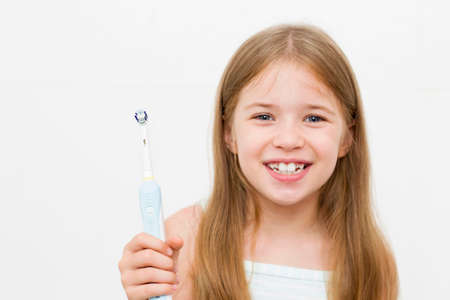 The girl cleans her teeth with an electric brush. Morning hygiene procedures. A beautiful smile. White teeth.の写真素材