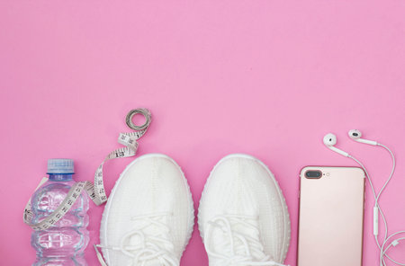 A fitness concept with a water bottle, sneakers, a phone with headphones, a pink roller on a pink background. A place to copy.の写真素材