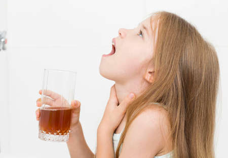 The girl is choking with medicine in the bathroom. Angina tonsillitis. Covid-19の写真素材