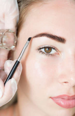 Young woman correcting eyebrow shape with brush, closeupの写真素材