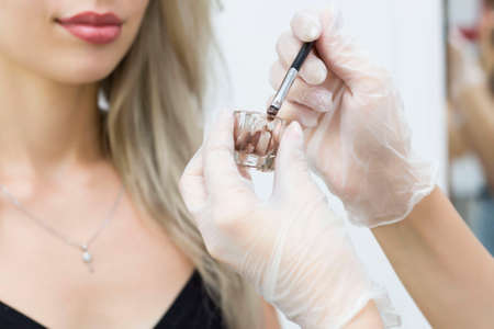 A young girl is undergoing a procedure for correcting and coloring her eyebrows. Master of cooking henna in a special cup.の写真素材