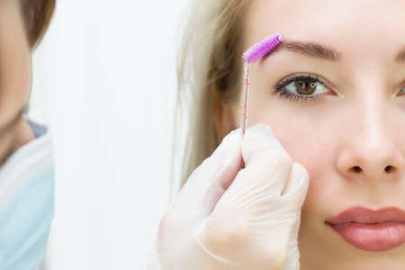 A young woman combs her eyebrows with a pink brush. Eyebrow correction, henna staining. Close-up. Half of the face.の写真素材