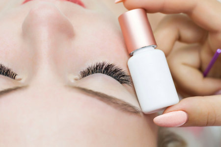 A closed eye with extended eyelashes and a tube of glue, primer next to it. Glue for eyelash...
