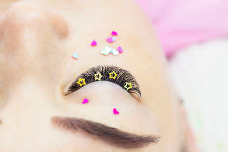 The master of eyelash extension decorates the girl's eyelashes with rhinestones, hearts and stars. Creative eyelash extensions, eye makeup.の写真素材