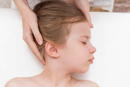 a seven-year-old girl at an appointment with an osteopath. Pediatric osteopathy. Headaches in school-age children. Correction of the skull, spine.の写真素材