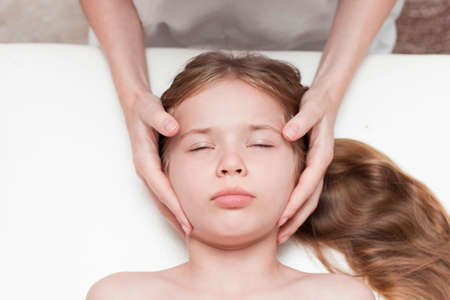 a seven-year-old girl at an appointment with an osteopath. Pediatric osteopathy. Headaches in school-age children. Correction of the skull, spine.の写真素材