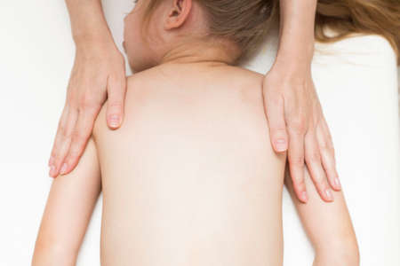 The hands of the masseur do a back massage for a girl of primary age. Spine. Back pain in school-age children.の写真素材