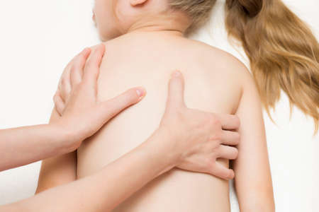 The hands of the masseur do a back massage for a girl of primary age. Spine. Back pain in school-age children.の写真素材