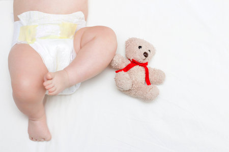 The baby is lying on a white sheet and next to Teddy bear. Legs of a newborn close-up.の写真素材