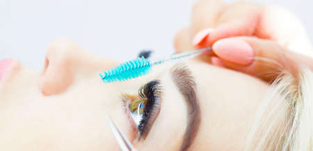 The girl is undergoing an eyelash extension procedure. Beautiful close-up of the eyes and turquoise brush. The concept of artificial eyelashes, a trend.の写真素材