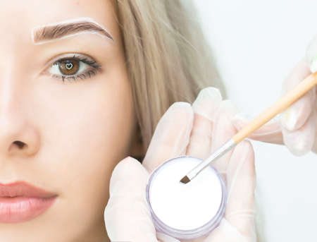 The makeup artist makes notes with a white eyebrow pencil and paints eyebrows. Professional makeup and facial care. Eyebrow correction, henna staining. Permanent makeup.の写真素材