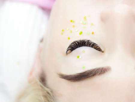 The girl is undergoing an eyelash extension procedure. Beautiful black and long eyelashes. Rhinestones green stars under the eyes. Decorの写真素材