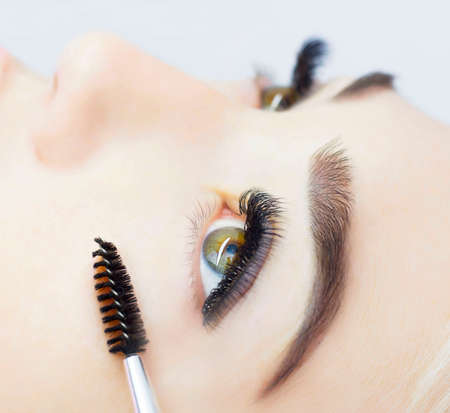 The girl is undergoing an eyelash extension procedure. Beautiful close-up of the eyes, thick black eyelashes. The concept of artificial eyelashes, a trend.の写真素材