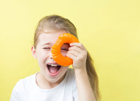anti-stress sensory plastic toy made of pop tube in the hands of a child. A joyful girl is playing at home with a toy-a fidget pop tube. the trend of 2021. Yellow backgroundの写真素材