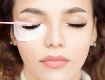Beautiful girl with long artificial eyelashes. Eyelash extension procedure. Pink brush combs eyelashes.の写真素材