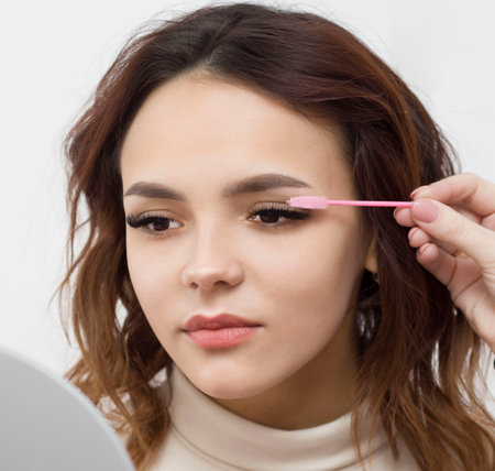 A beautiful girl on an eyelash extension procedure, a female eye with long eyelashes is combed with a pink brush. Eyelashes, close-up, macro, selective focus.の写真素材