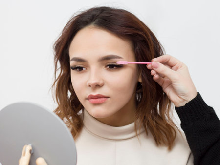 A beautiful girl on an eyelash extension procedure, a female eye with long eyelashes is combed with a pink brush. Eyelashes, close-up, macro, selective focus.の写真素材