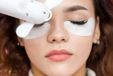 Eyelash extensions. a young woman undergoes a close-up eyelash extension procedure. The master dries the eyelashes after the procedure with a fan.の写真素材