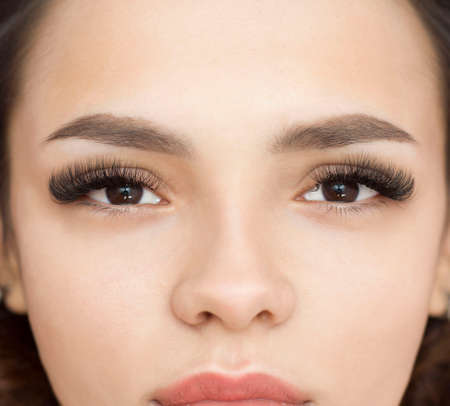 Eyelash extensions. Close-up of the face of a beautiful girl with thick black artificial eyelashes. Macro.の写真素材