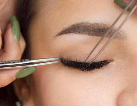Eyelash extensions. a young woman undergoes a close-up eyelash extension procedure. Tweezers.の写真素材