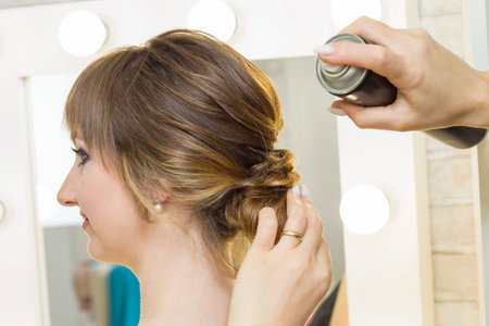 The stylist performs the hairstyle, hair styling in the salon. Splashes hairspray.