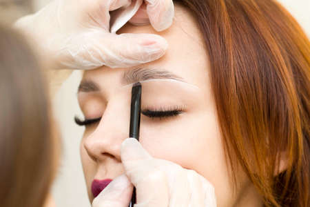 The makeup artist makes markings with a white eyebrow pencil and paints eyebrows. Professional makeup and facial care. permanent makeupの写真素材