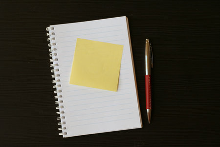 White lined scratchpad (notepad) with yellow postit card and red pen on a black wooden table