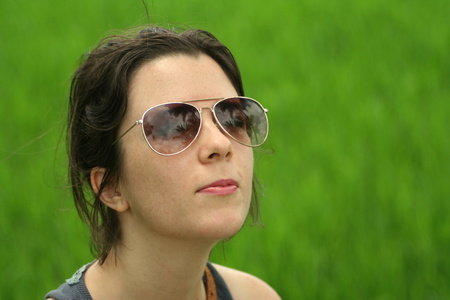 Freckled caucasian brunette girl with sunglasses looking up to the sun. Green grass in the background. Natural facial expression.の写真素材